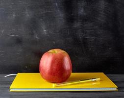 red ripe apple lies on a yellow closed notebook photo