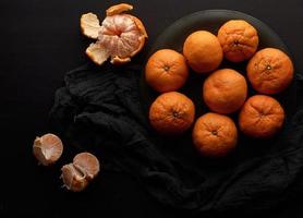 muchas mandarinas enteras redondas maduras naranjas en un plato sobre una mesa de madera negra foto