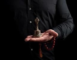 un hombre adulto con una camisa negra sostiene una campana ritual tibetana de cobre, de bajo perfil foto