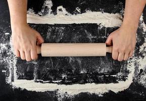 wooden rolling pin in female hands on a black background with white wheat flour photo