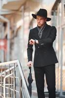 Elegant young man in black hat and with umbrella outdoors in the city photo