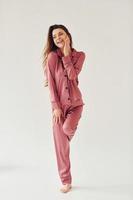 Cheerful young woman in pajamas standing indoors against white background in the studio photo