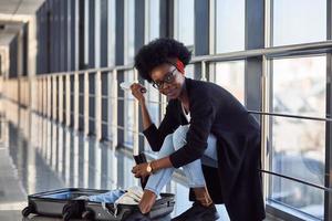 Young african american female passanger in casual wear is in airport with baggage packing clothes photo