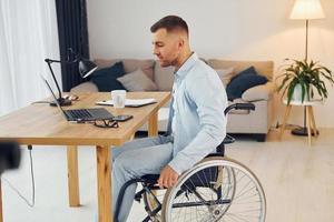 Working by using laptop. Disabled man in wheelchair is at home photo