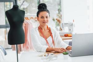 Sitting by the table. Seamstress is in her office that is with different clothes photo