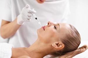 Close up of hands of cosmetologist making botox injection in female lips photo