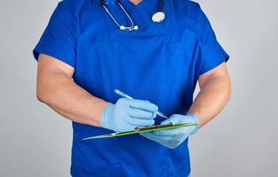 doctor in blue uniform and sterile latex gloves holds clipboard with a blank sheet of paper photo