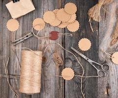 una bobina de cuerda marrón, etiquetas de papel y tijeras viejas sobre un fondo de madera gris foto