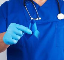 doctor in blue uniform and sterile latex gloves holds a dark blue ribbon, concept of timely research photo