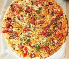 baked round pizza with smoked sausages, mushrooms, tomatoes, cheese and dill in an open cardboard box photo