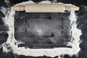 wooden rolling pin on a black background, scattered white wheat flour photo