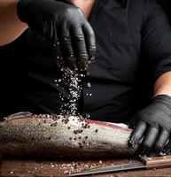 chef in a black shirt and black latex gloves prepares salmon fillet on a wooden cutting board photo