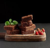 stack of baked square pieces of chocolate brownie cake on brown wooden cutting board photo