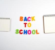 inscripción de regreso a la escuela con letras plásticas multicolores y una pila de cuadernos con hojas blancas en blanco foto