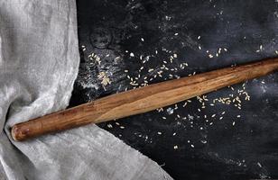 very old wooden rolling pin on a black background, near a gray linen towel photo