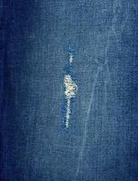 fragment of blue jeans fabric with a hole, full frame photo