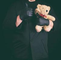 hombre vestido de negro sosteniendo un oso de peluche marrón foto