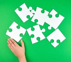 female hand puts empty white big puzzles on a green background photo