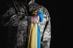 Ukrainian soldier holds in his hand the yellow-blue flag of the state, he pressed his hand to his chest photo