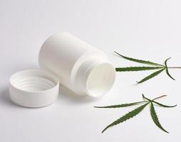 open empty white plastic medical jar for pills and green hemp leaf photo