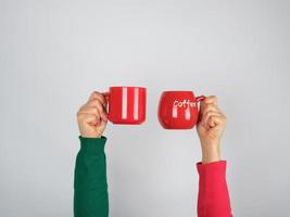 two hands in a sweater holding red ceramic mugs photo