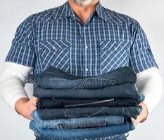 man in jeans and blue plaid shirt holding a pile of jeans photo