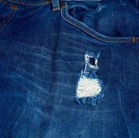 fragment of blue jeans fabric with a hole photo