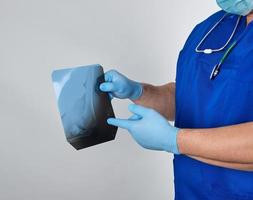 doctor in blue uniform and sterile latex gloves holds and examines X-ray of leg bone photo
