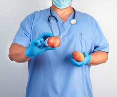 médico con uniforme azul y guantes de látex estériles sostiene manzanas rojas maduras foto