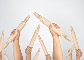 many hands raised up and holding kitchen wooden rolling pins photo