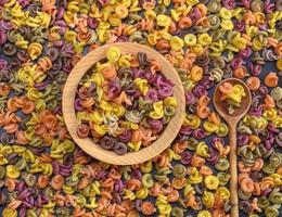 multicolored spiral raw pasta fusilli in a wooden bowl photo