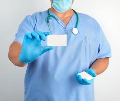 doctor in sterile latex gloves and blue uniform holds a blank white business card photo