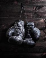 pair of very old shabby black leather boxing gloves hanging on a nail photo
