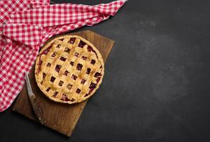 baked round pie with plums on a black background, top view. Place for inscription photo