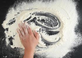 white wheat flour scattered on a black background, product is spread over the surface photo