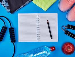 open empty notebook and  women's clothing for sports and fitness, top view, blue background photo