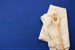 cuchara de madera vintage y toalla de cocina textil blanca sobre fondo de madera azul foto