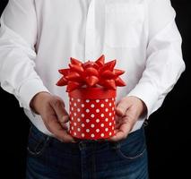 adult man in a white shirt holds a round gift cardboard box with a bow photo