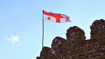 vista estática de la antigua bandera georgiana ondeando en cámara lenta con las ruinas históricas del edificio del pueblo de samshvilde video