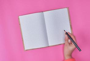 open notebook in a cell and a female hand holding a black wooden pencil photo