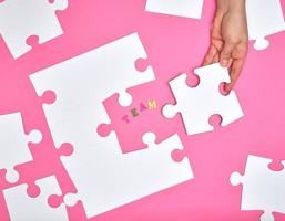 female hand puts white big puzzles on a pink background photo