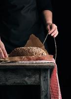 girl in black clothes wraps a whole baked loaf of bread in brown kraft paper photo