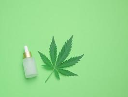 White glass bottle with pipette and green cannabis leaf on a green background photo