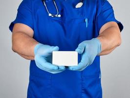 doctor in sterile latex gloves and blue uniform holds a blank white business card photo