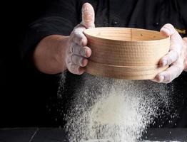 man sifts white wheat flour through a wooden sieve photo