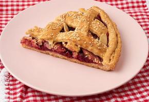 triangular slice of baked cherry pie on a pink round plate photo