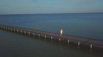 Eine Frau geht auf einem Holzsteg in der Nähe des Meeres video