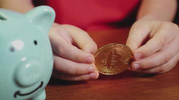 The child puts a bitcoin gold coin in a piggy bank video