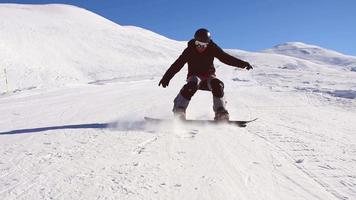 vue latérale statique snowboarder vêtu de vêtements de sport noir foncé descendant la pente de la montagne et taillé en géorgie, goderdzi le jour ensoleillé du caucase video