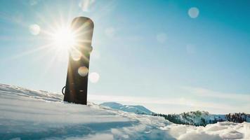 Close up black base of snowboard in snow with white mountains in the background. Skiing snowboarding banner vertical panorama video